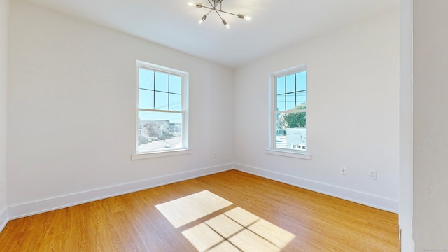 unfurnished room with wood-type flooring, a notable chandelier, and a healthy amount of sunlight