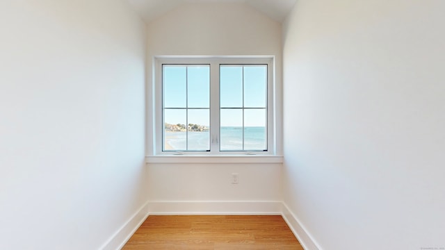 unfurnished room with a water view, vaulted ceiling, and light wood-type flooring