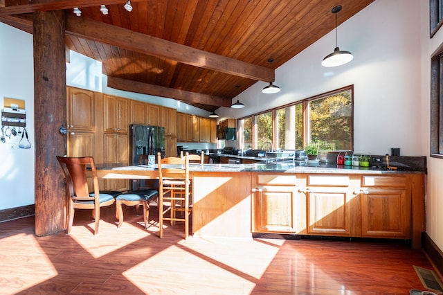 kitchen with kitchen peninsula, black fridge, high vaulted ceiling, dark hardwood / wood-style floors, and hanging light fixtures