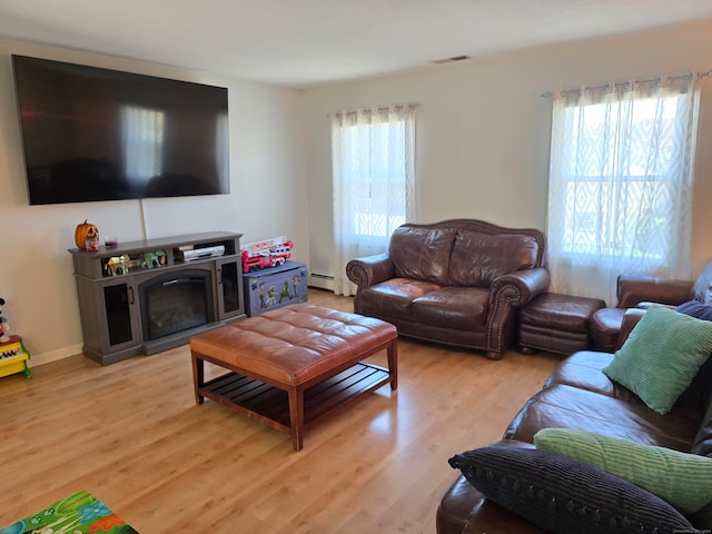 living room with baseboard heating, light hardwood / wood-style floors, and a healthy amount of sunlight