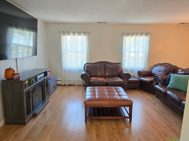 living room featuring baseboard heating, light hardwood / wood-style flooring, a textured ceiling, and plenty of natural light