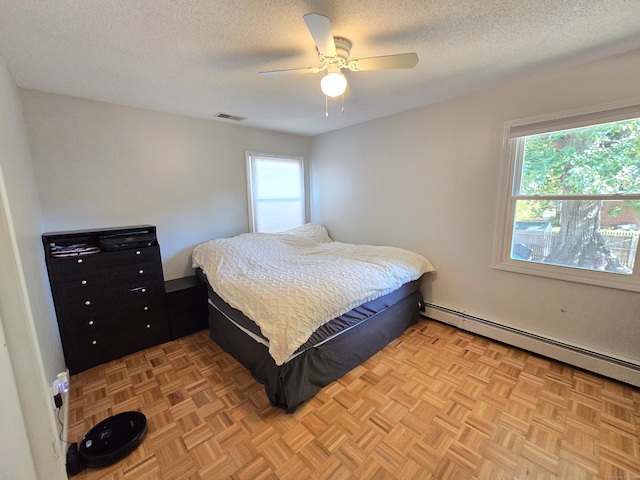 bedroom with a textured ceiling, a baseboard heating unit, multiple windows, and ceiling fan