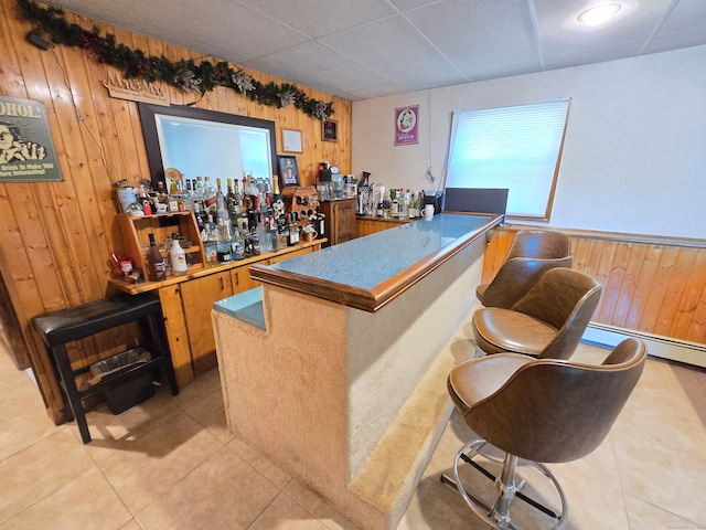 bar with a baseboard radiator, a paneled ceiling, wood walls, and light tile patterned floors