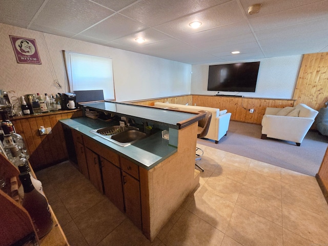 kitchen with a breakfast bar area, sink, wooden walls, and a drop ceiling