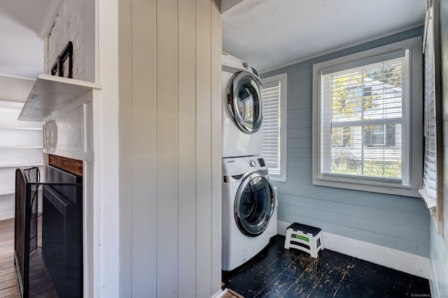 clothes washing area featuring hardwood / wood-style floors, wooden walls, and stacked washing maching and dryer