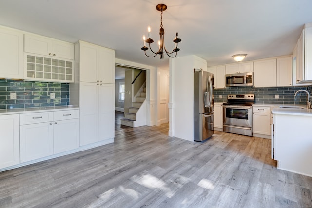 kitchen featuring light wood-type flooring, pendant lighting, tasteful backsplash, stainless steel appliances, and white cabinets