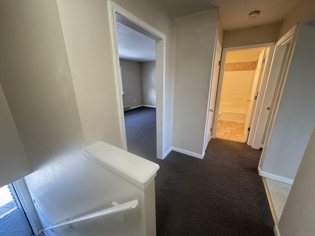 corridor featuring baseboards, dark colored carpet, and a textured ceiling