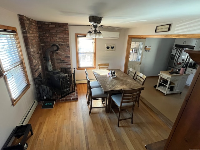 dining room featuring light wood-type flooring, a baseboard heating unit, a wood stove, and plenty of natural light