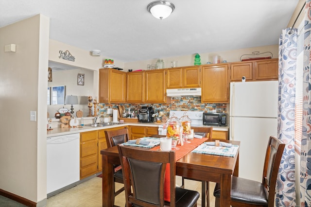 kitchen featuring a sink, tasteful backsplash, white appliances, light countertops, and under cabinet range hood