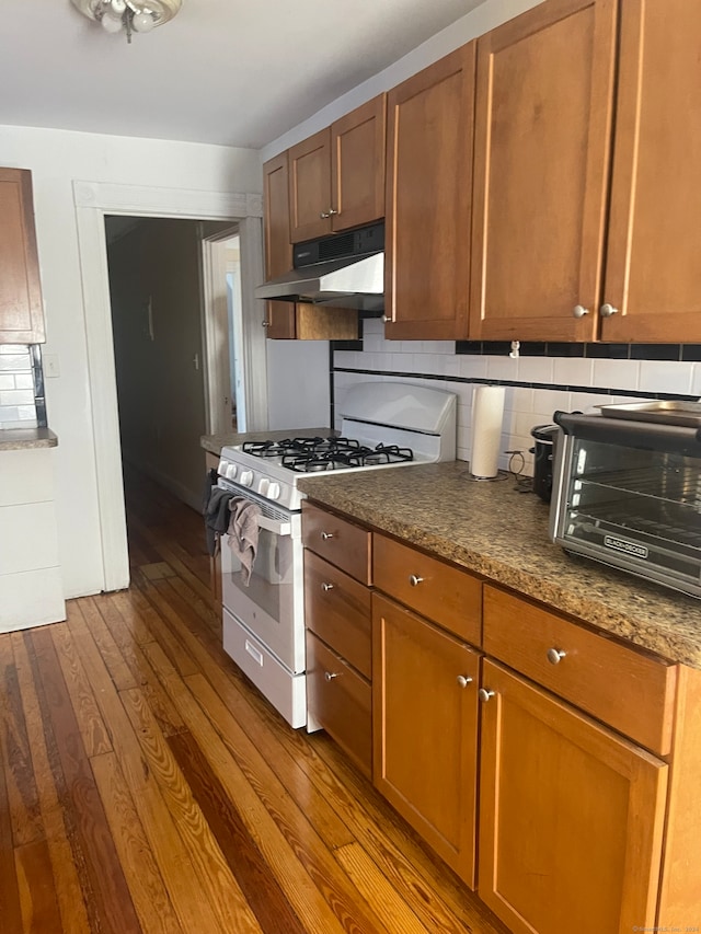 kitchen with tasteful backsplash, white range with gas cooktop, dark stone countertops, and wood-type flooring