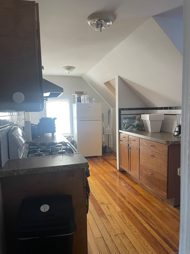 kitchen with backsplash, gas range oven, exhaust hood, white refrigerator, and light hardwood / wood-style floors