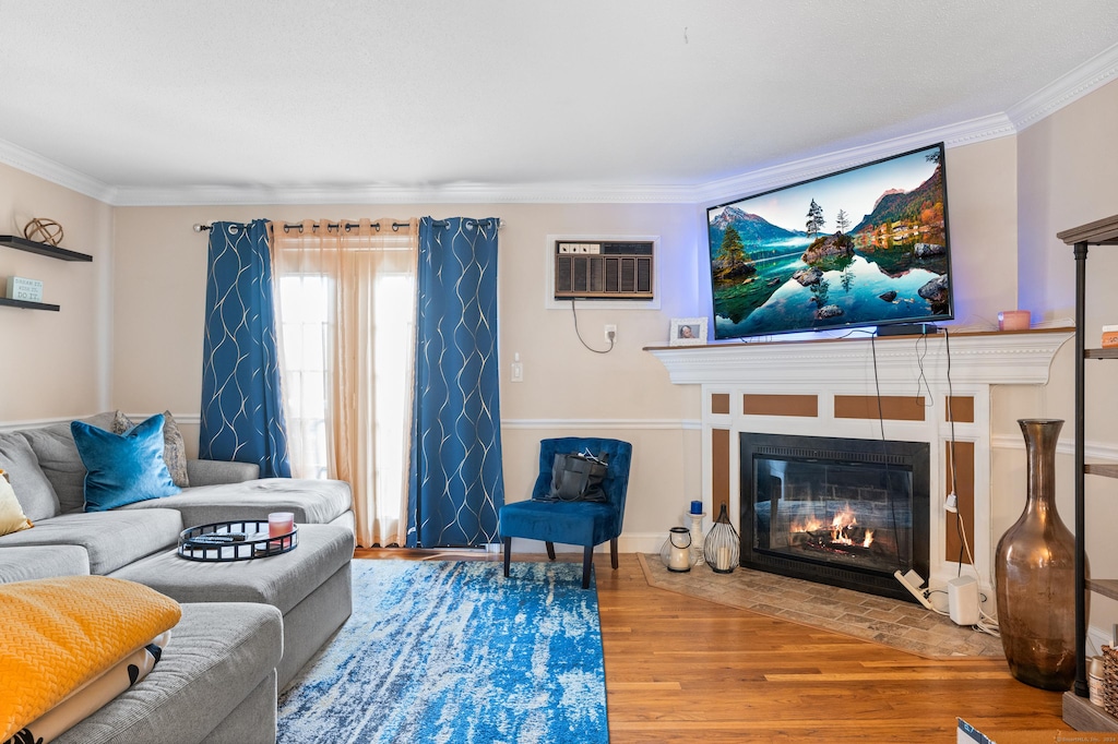 living room with a wall unit AC, ornamental molding, and hardwood / wood-style flooring