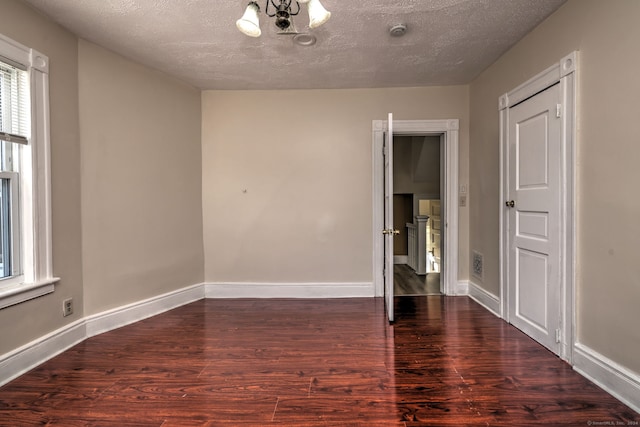 unfurnished room with a notable chandelier, dark wood-type flooring, and a textured ceiling