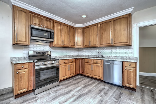 kitchen with light stone countertops, a textured ceiling, appliances with stainless steel finishes, sink, and light wood-type flooring