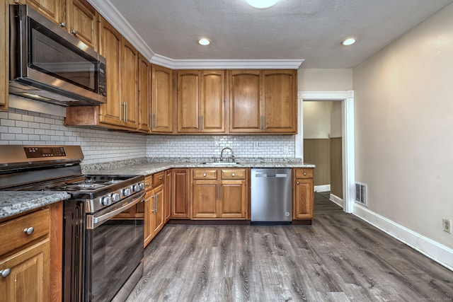 kitchen with sink, light stone counters, appliances with stainless steel finishes, and dark wood-type flooring