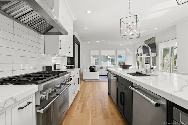 kitchen featuring a healthy amount of sunlight, appliances with stainless steel finishes, wall chimney range hood, and white cabinets