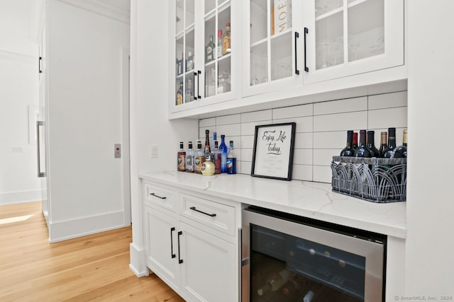 bar with decorative backsplash, light hardwood / wood-style flooring, light stone countertops, beverage cooler, and white cabinets