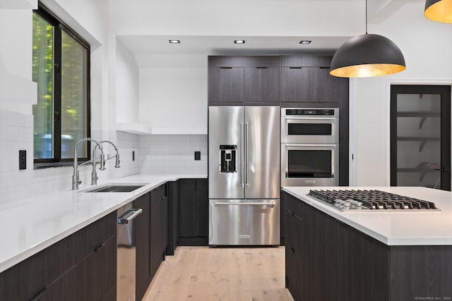 kitchen with sink, hanging light fixtures, stainless steel appliances, light hardwood / wood-style flooring, and decorative backsplash