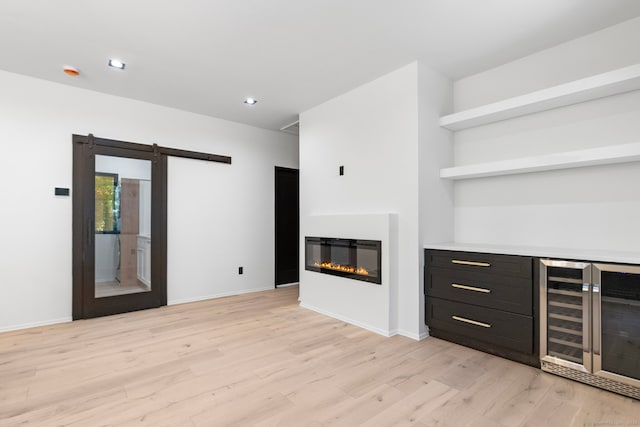 unfurnished living room with light wood-type flooring, wine cooler, and a barn door