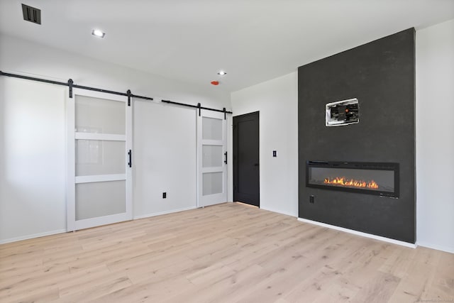 unfurnished bedroom with a fireplace, light wood-type flooring, and a barn door