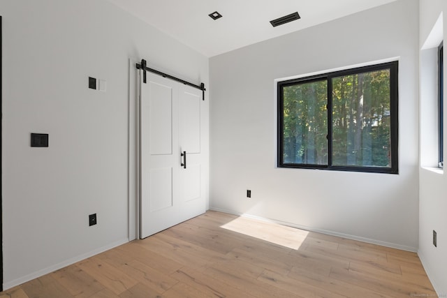 unfurnished bedroom featuring a barn door and light hardwood / wood-style floors