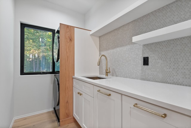 kitchen featuring backsplash, stacked washing maching and dryer, sink, light hardwood / wood-style flooring, and white cabinetry