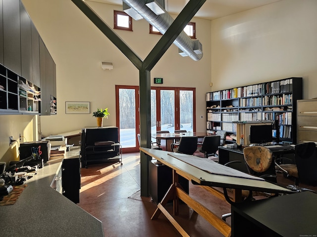 home office featuring a towering ceiling, french doors, and concrete flooring