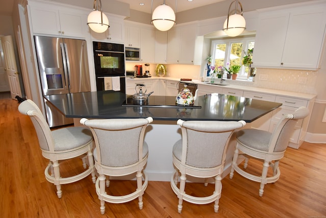 kitchen with decorative light fixtures, stainless steel appliances, a center island, and white cabinetry