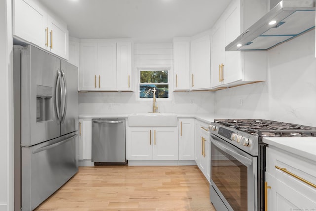 kitchen with sink, wall chimney exhaust hood, light wood-type flooring, white cabinetry, and stainless steel appliances