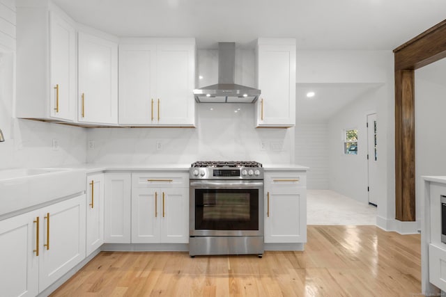 kitchen featuring wall chimney exhaust hood, white cabinetry, light hardwood / wood-style flooring, and stainless steel gas range