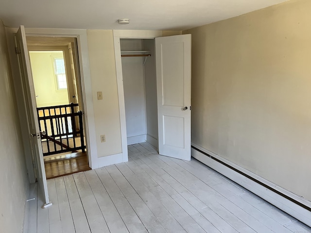 unfurnished bedroom featuring baseboard heating, light wood-type flooring, a closet, and baseboards