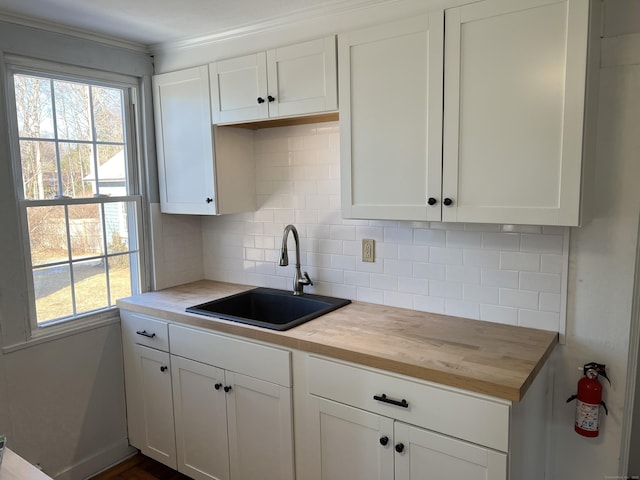 kitchen with backsplash, white cabinetry, a sink, and wood counters