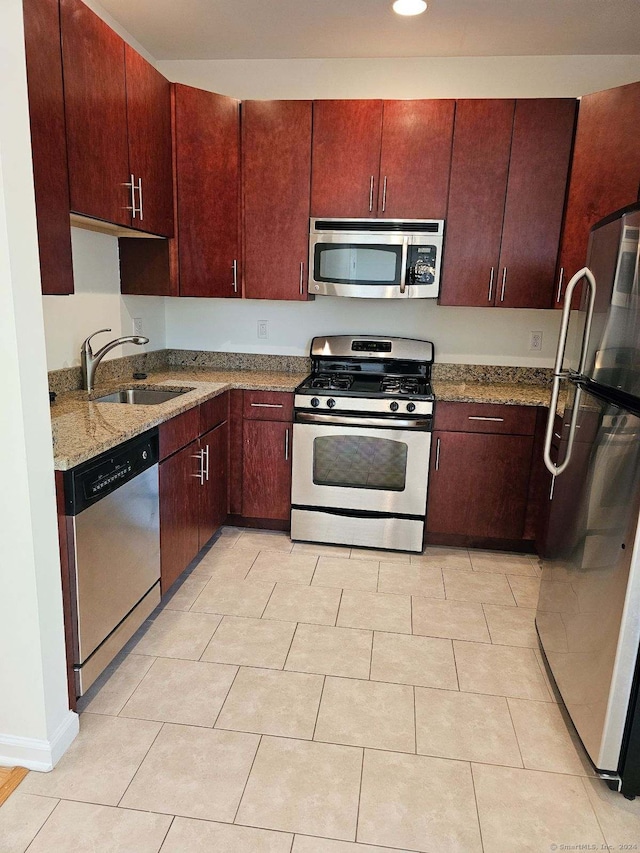 kitchen with sink, appliances with stainless steel finishes, light tile patterned floors, and dark stone countertops