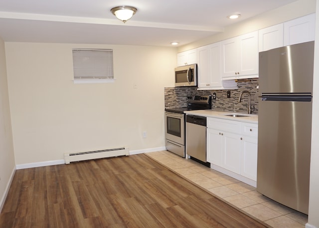 kitchen with a baseboard heating unit, stainless steel appliances, sink, white cabinetry, and light hardwood / wood-style floors