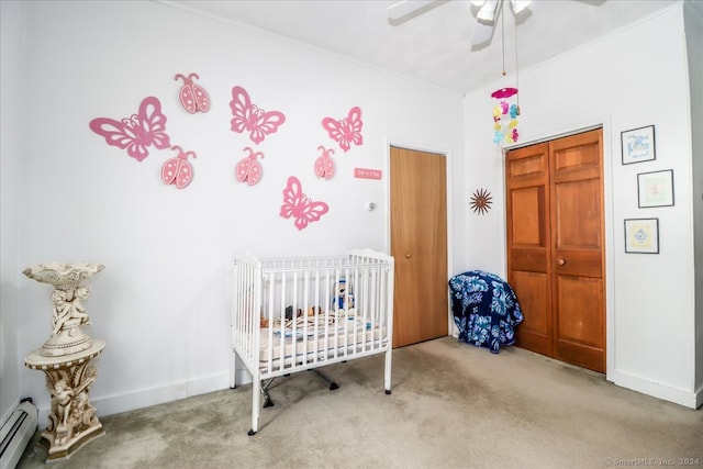 carpeted bedroom with ceiling fan, a crib, a closet, and a baseboard heating unit