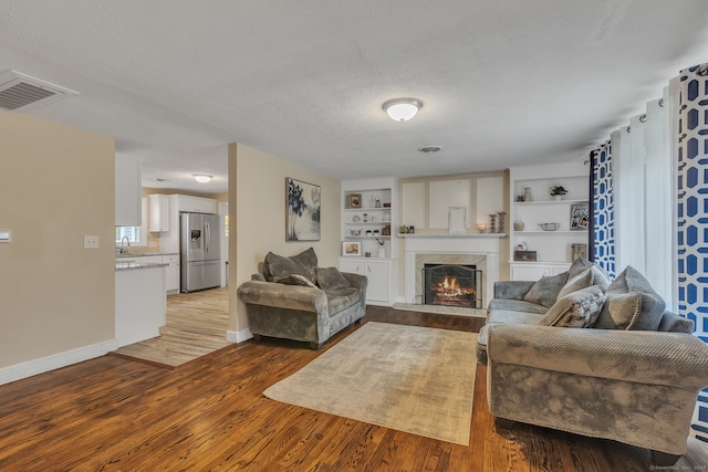 living room with built in shelves, light wood-type flooring, sink, a fireplace, and a textured ceiling