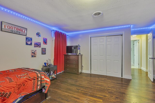 bedroom with wood finished floors, baseboards, visible vents, a closet, and a textured ceiling