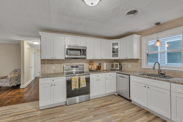 kitchen featuring visible vents, stainless steel appliances, light wood-style floors, white cabinetry, and a sink