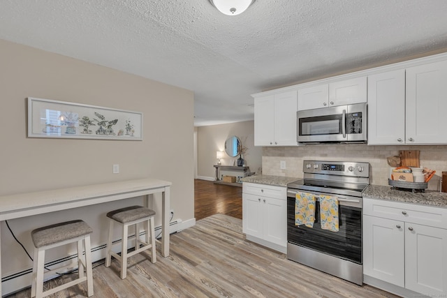 kitchen featuring light wood finished floors, backsplash, light stone counters, stainless steel appliances, and white cabinetry