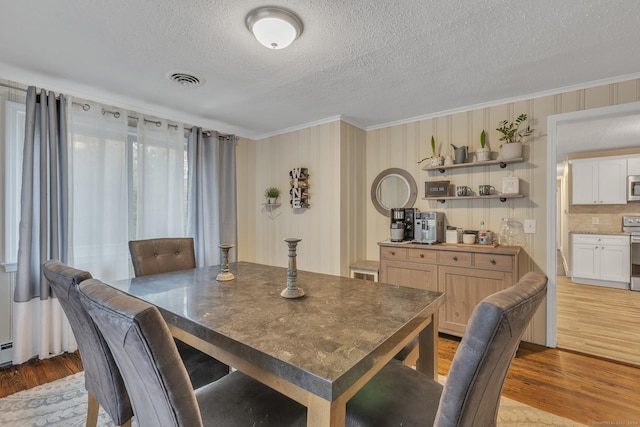 dining space with a textured ceiling, wood finished floors, and ornamental molding