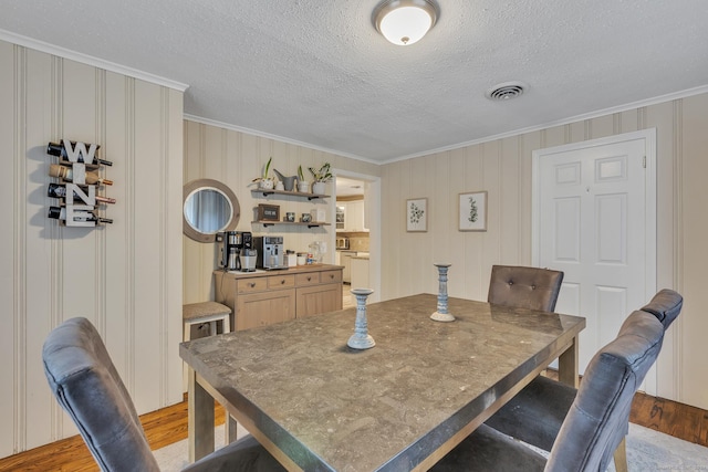 dining room featuring crown molding, visible vents, light wood finished floors, and a textured ceiling