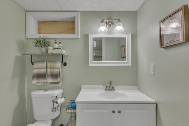 half bathroom featuring a drop ceiling, toilet, and vanity