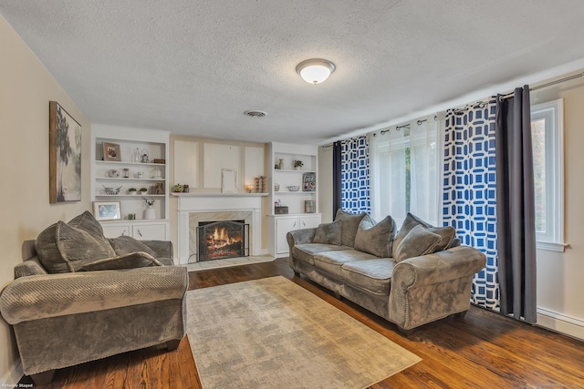 living area featuring a high end fireplace, visible vents, built in shelves, a textured ceiling, and dark wood-style flooring