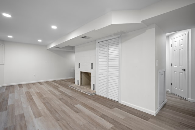 basement featuring a large fireplace and light hardwood / wood-style floors