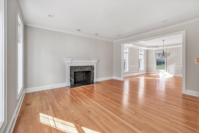 unfurnished living room with an inviting chandelier, ornamental molding, and light wood-type flooring