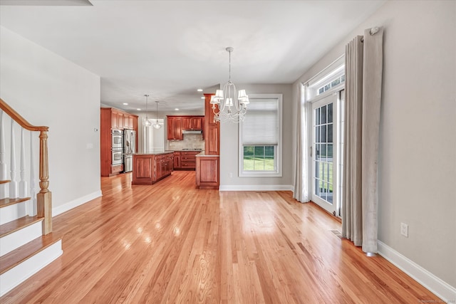 kitchen with light wood-type flooring, a kitchen island, hanging light fixtures, stainless steel refrigerator, and a chandelier