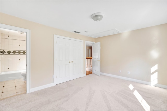 unfurnished bedroom with a closet, ensuite bath, and light colored carpet