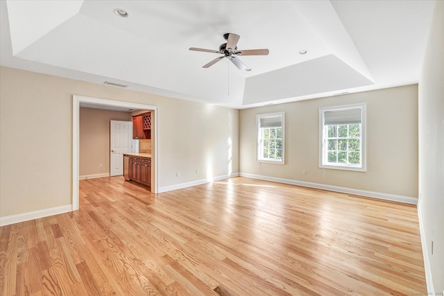 unfurnished living room featuring a raised ceiling, light wood-type flooring, and ceiling fan