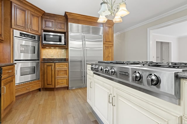 kitchen with ornamental molding, stainless steel appliances, decorative light fixtures, a chandelier, and light hardwood / wood-style floors