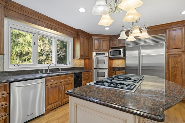 kitchen featuring built in appliances, sink, a center island, and hanging light fixtures